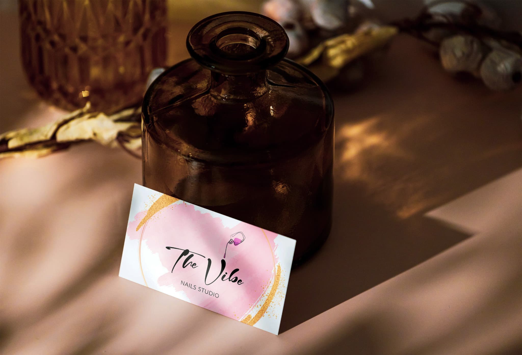 THE VIBE business card with its pink and gold identity, styled beside a glass vase.